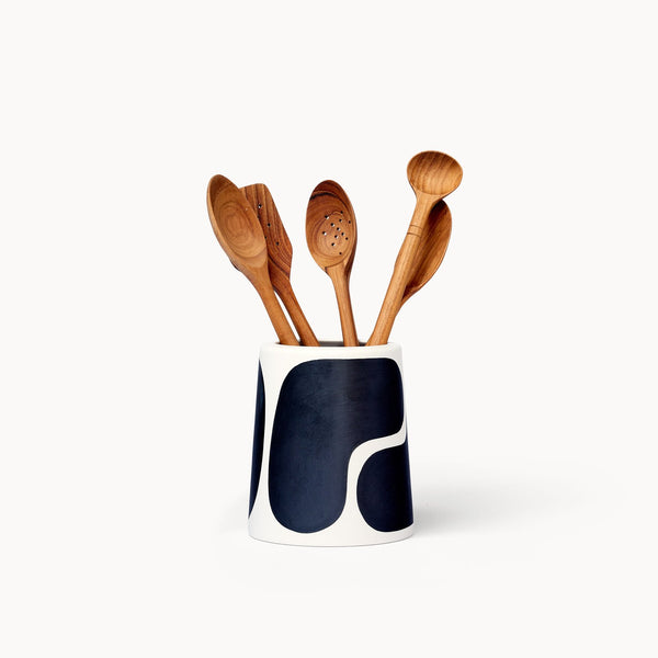 A vase in white with a black color block pattern, resembling mid-century design. Several wooden spoons are standing in the vessel.