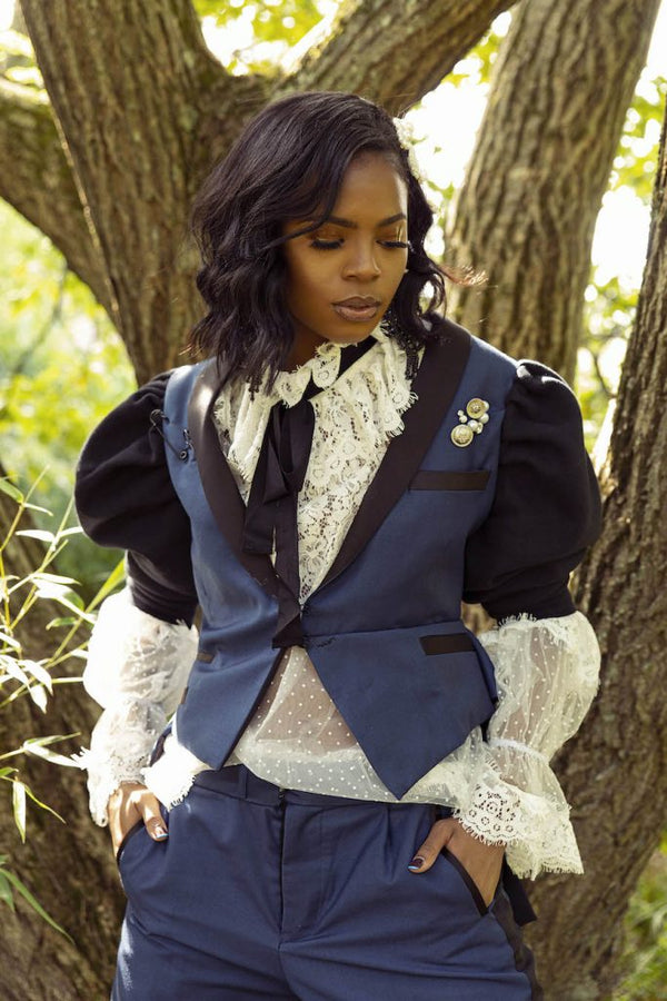 A photograph of a woman with a dark skin tone standing before a tree.
